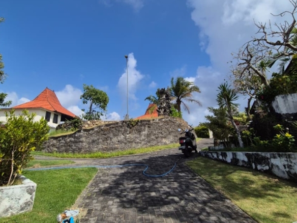 Melasti freehold plot, Bali: paved access road, stone retaining wall and Balinese-roofed pavilions